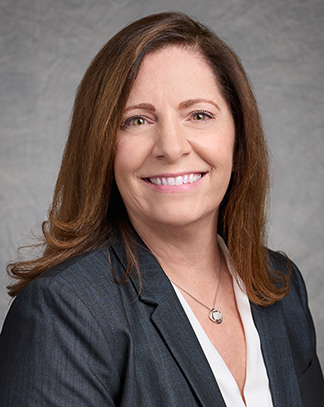 A professional headshot of Kathleen Cleary, a smiling woman with shoulder-length brown hair, wearing a gray blazer and sitting against a light gray background. The subject is facing the camera with a friendly and approachable expression.